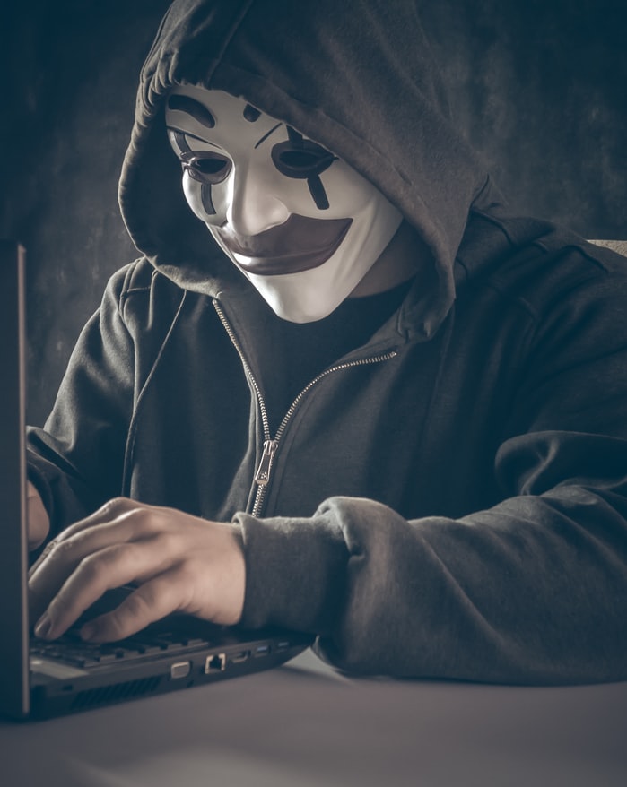 A hacker in mask typing on a computer.